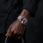 Pink-dial silver-tone Klaw watch worn on a wrist holding a bag