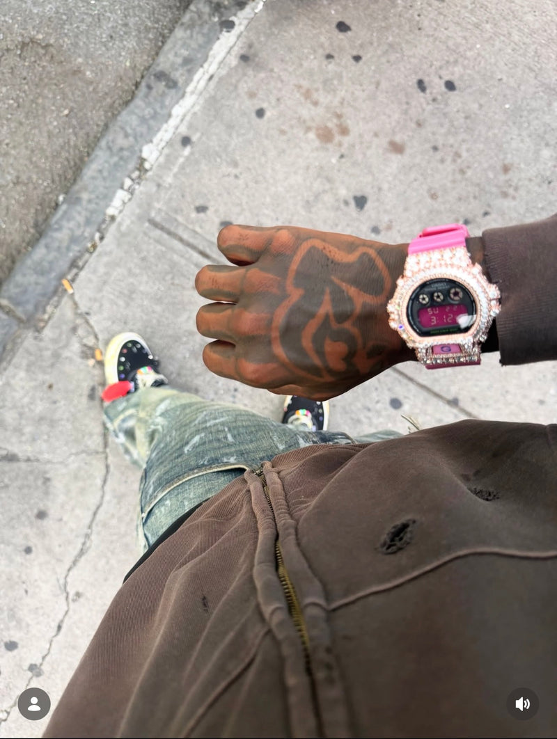 A pink digital watch with a stone-set bezel worn with a brown hoodie
